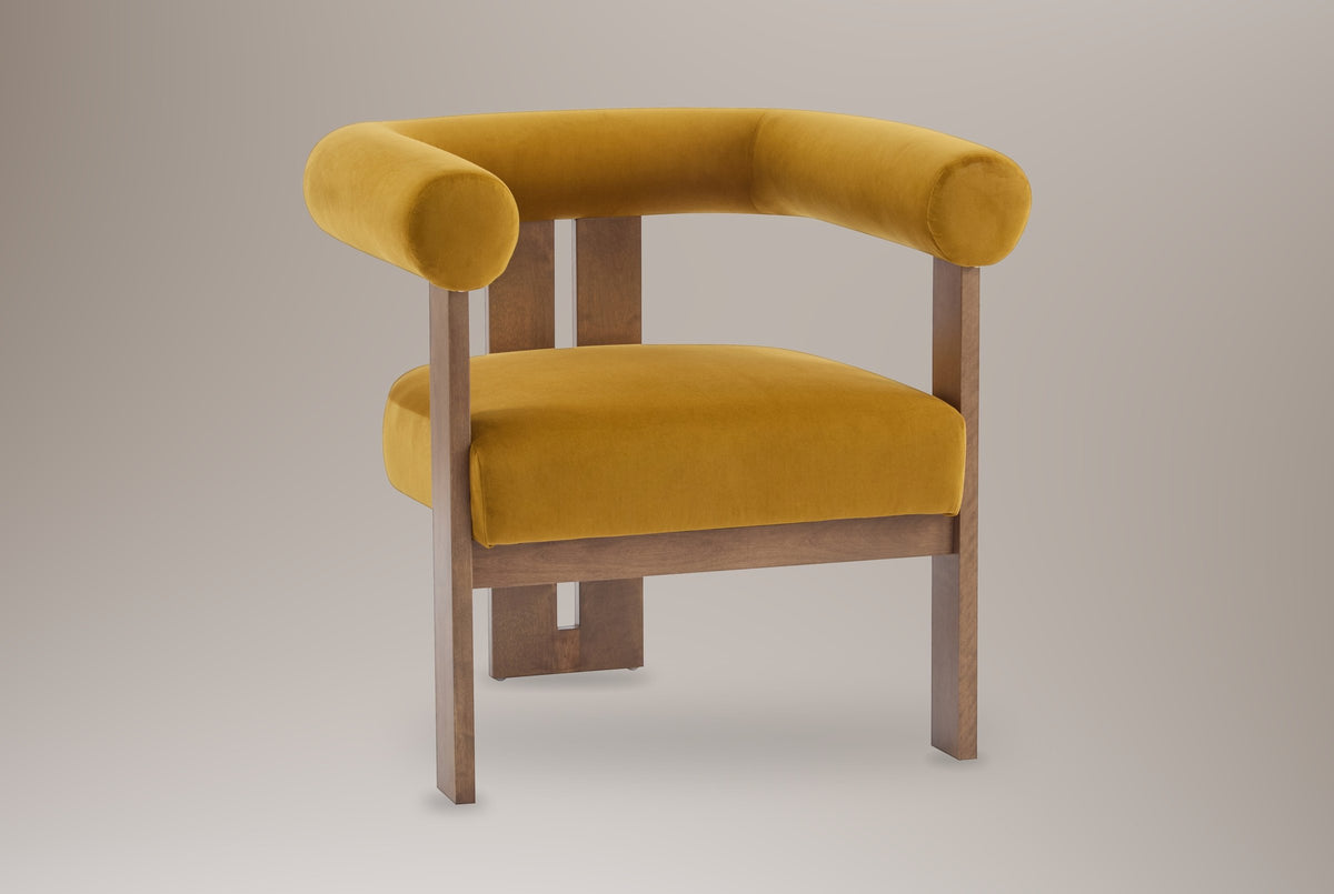 Caorle velvet round-arm accent chair in mustard yellow, three-quarter view on a warm grey studio backdrop
