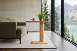 Side view of the Capalbio side table in Natural beside a moss green sofa in a Muncho Lake house