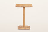 End view of the Capalbio side table in Natural on a warm white studio backdrop: a slim post centred on the plinth