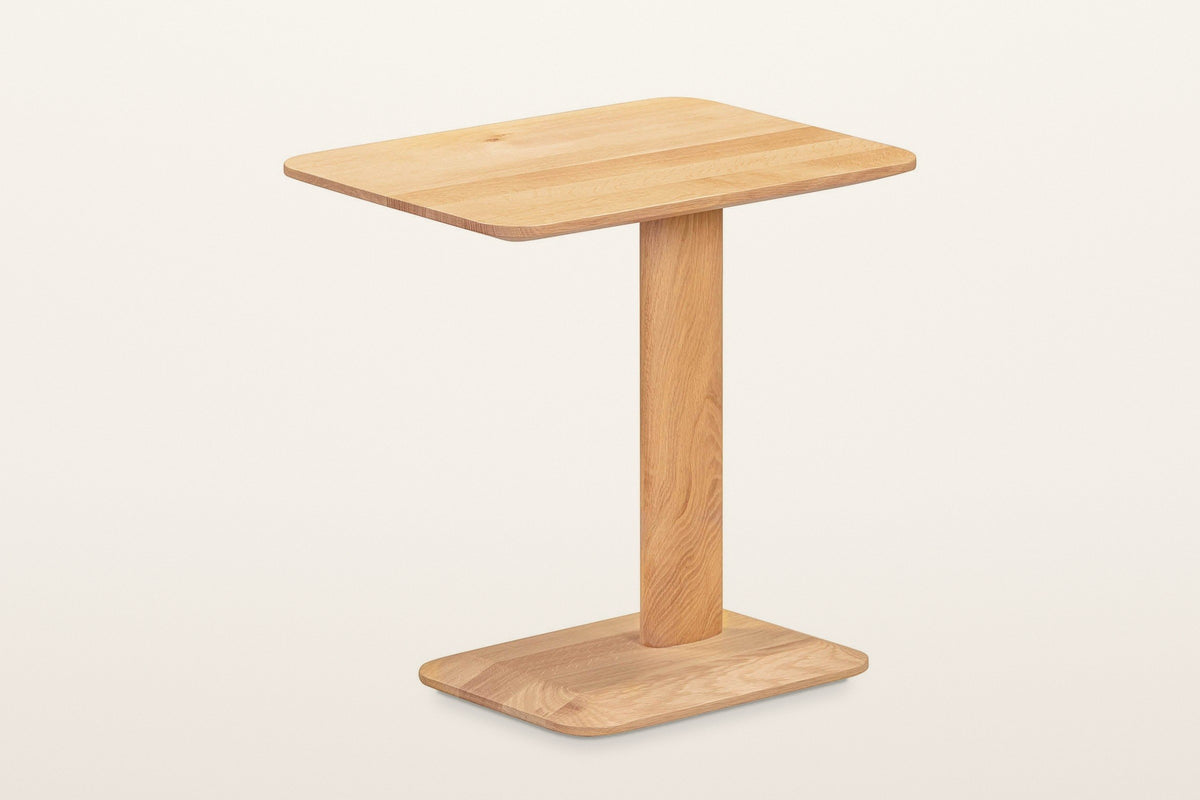 Capalbio oak side table in Natural, three-quarter view on a warm white studio backdrop: a rounded rectangular top on one off