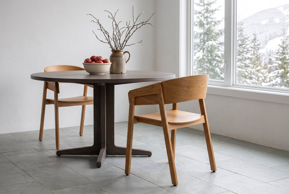 Two Caprarola dining armchairs in natural oak at a round smoked-oak pedestal table in a Whistler mountain home