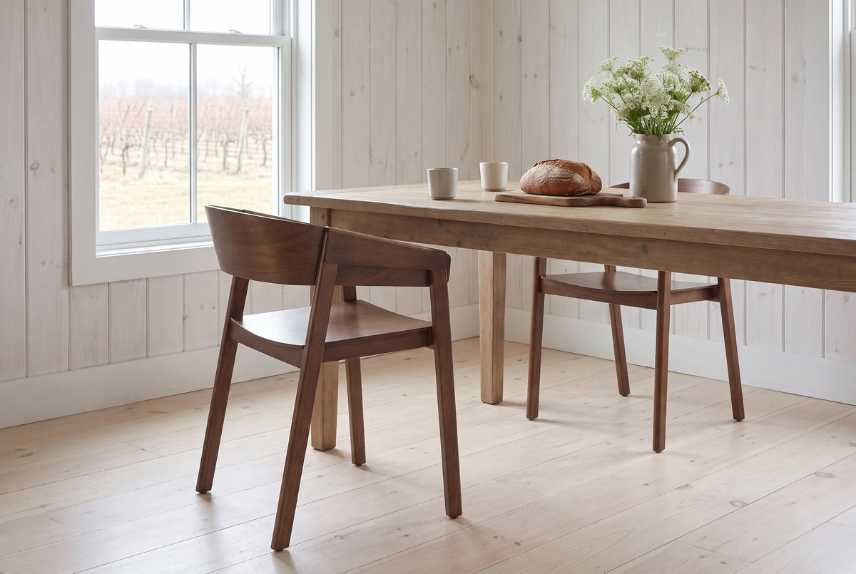 Two Caprarola dining armchairs in walnut at a scrubbed-pine farmhouse table in a Prince Edward County farmhouse