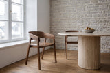 Two Caprarola dining armchairs in walnut at a round travertine pedestal table in a Quebec City stone house