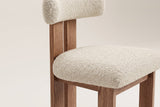 Close-up of a Carlo dining chair from above on an off-white backdrop: the ivory boucle seat and bolster backrest, the two wire-brushed oak back planks and the oak seat rail