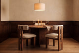 Three Carlo dining chairs in oak and ivory boucle tucked in around a round walnut table with two lit beeswax candles in brass holders, two glasses of red wine and a linen napkin, under a linen drum pendant, with dark oak panelling below a warm plaster wall in the evening