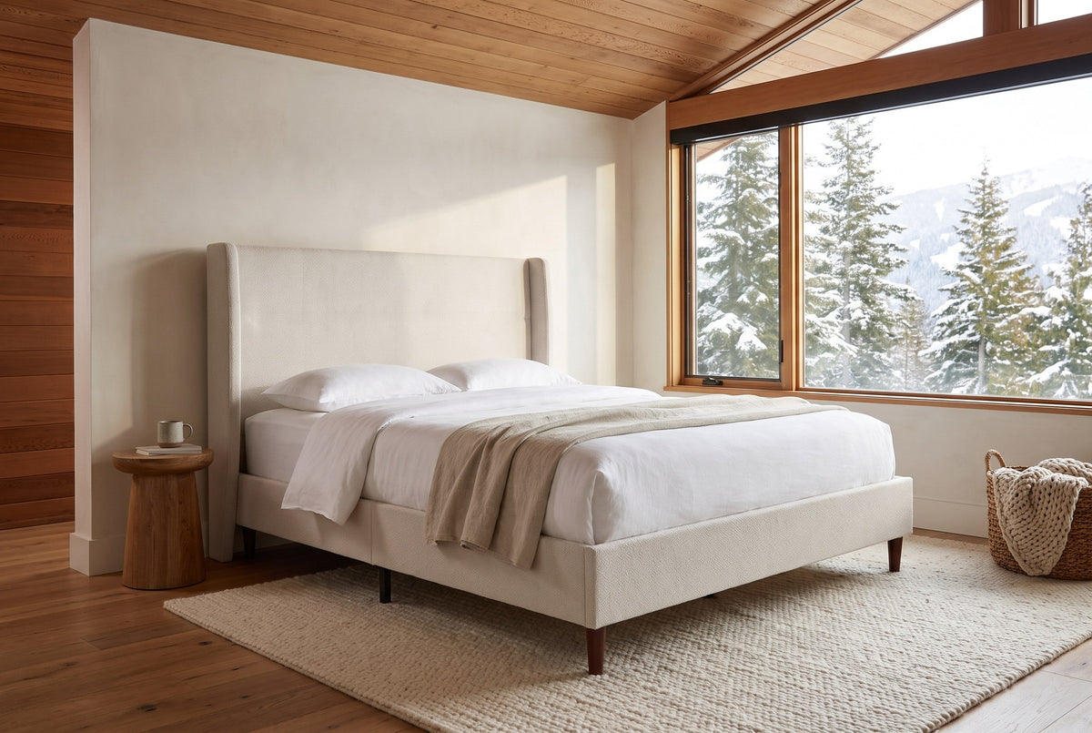 Carrara wingback bed in a chalet bedroom with a cedar ceiling, a wool rug and a window onto snowy firs and mountains