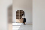 Woman opening the rattan doors of the Carver arched tall cabinet, showing its scale