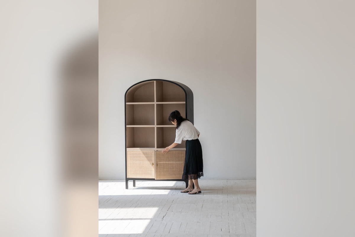 Woman opening the rattan doors of the Carver arched tall cabinet, showing its scale