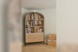 Carver arched cabinet filled with books and vases, with woven baskets beside it