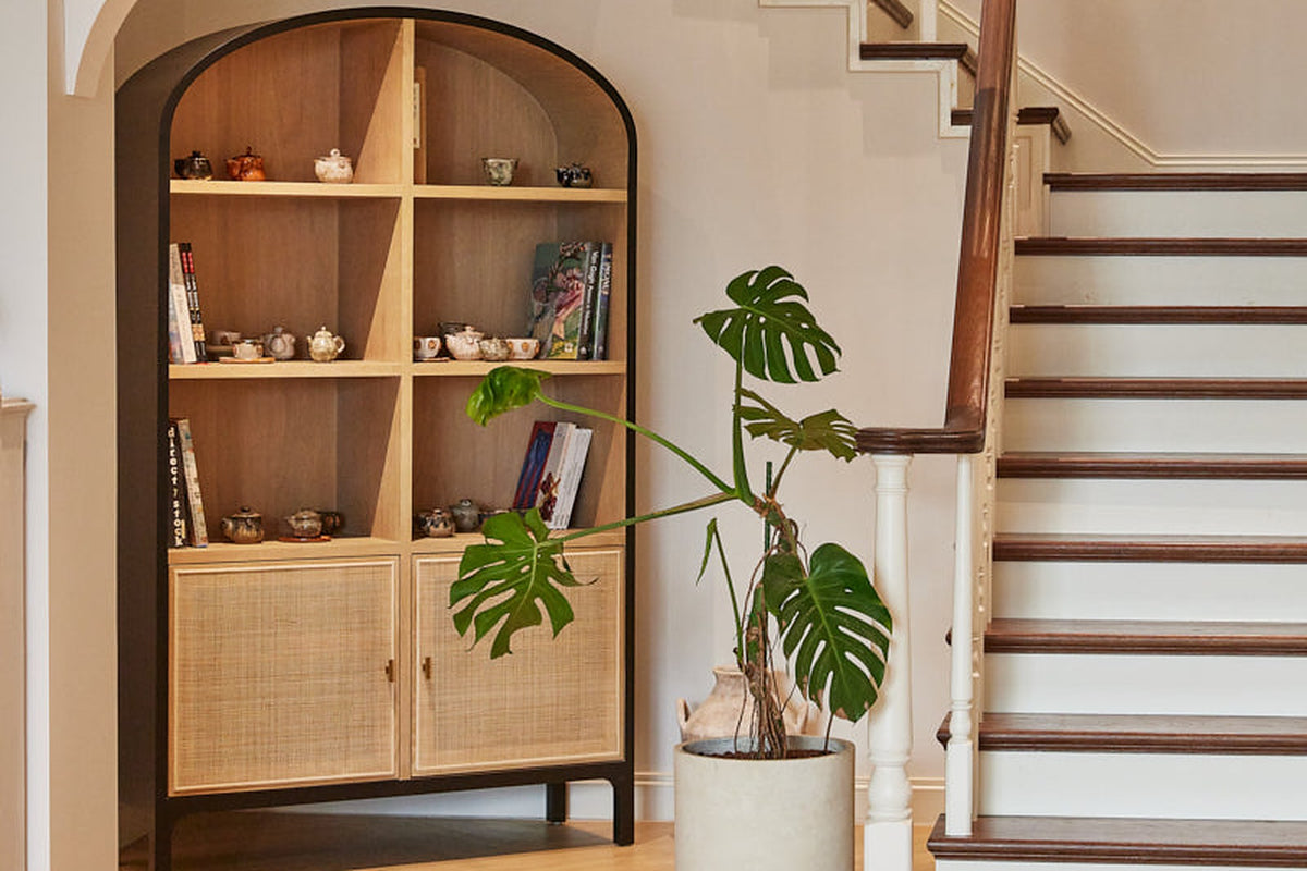 Carver arched tall cabinet in a hallway next to a staircase and potted plant