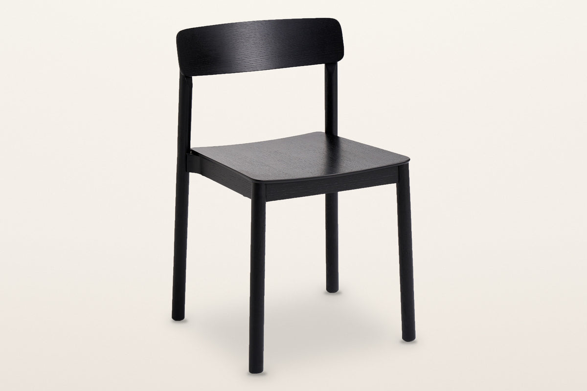 Casole stackable oak dining chair in black-stained oak, three-quarter view on a warm white studio backdrop