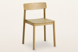 Casole stackable oak dining chair in natural oak, three-quarter view on a warm white studio backdrop