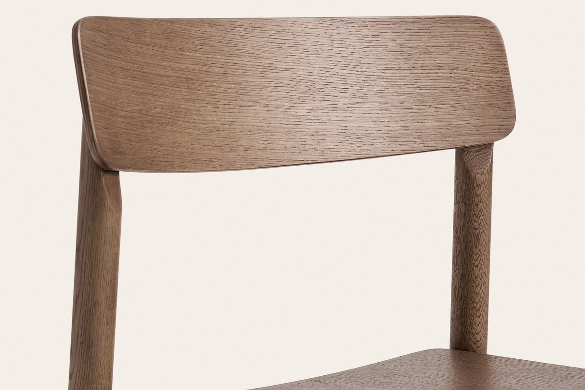 Close-up of the Casole back panel and rear post in walnut-stained oak: open oak grain and a softly rounded corner