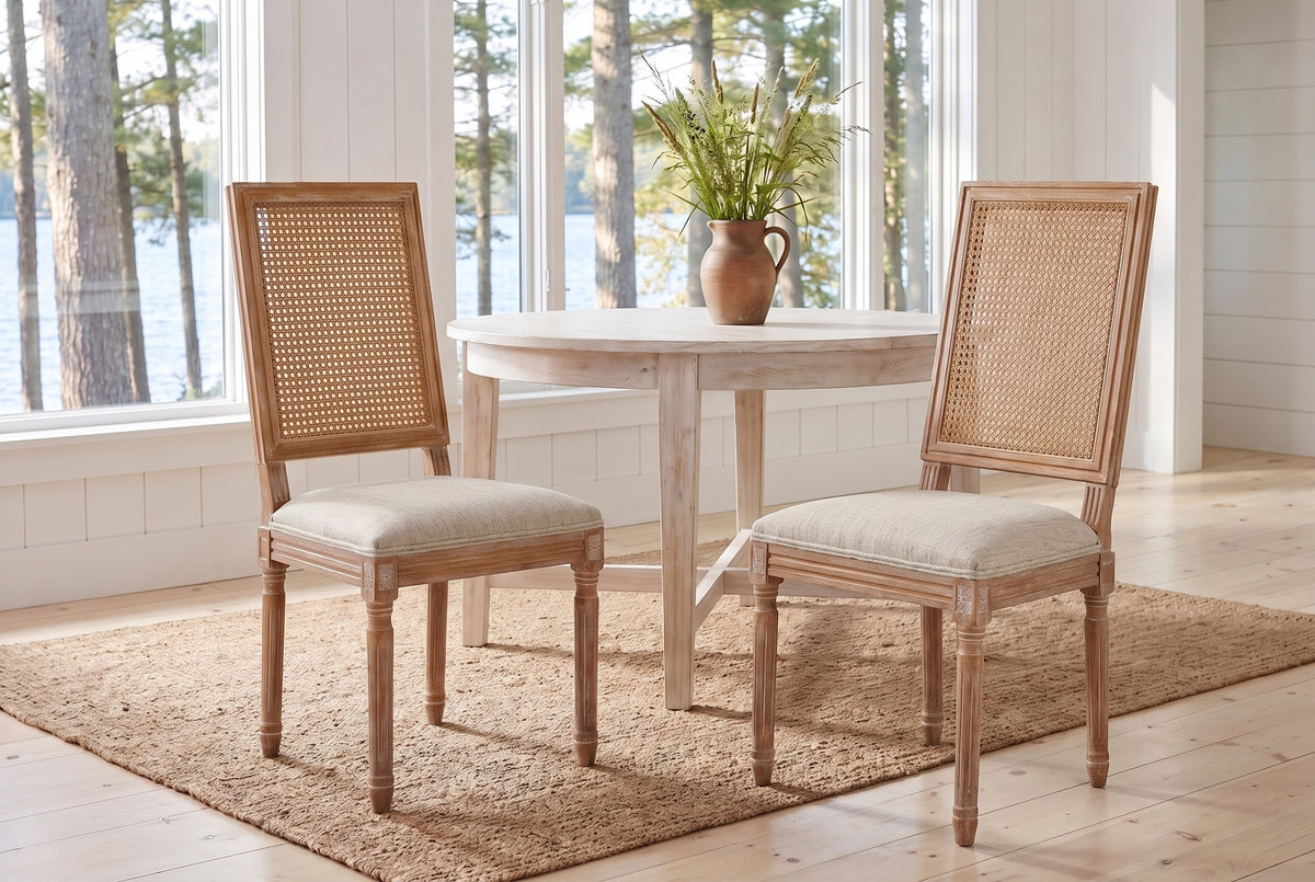 A pair of Castelfranco dining chairs in Beige on a jute rug in a white Muskoka cottage with a round table and the lake behind