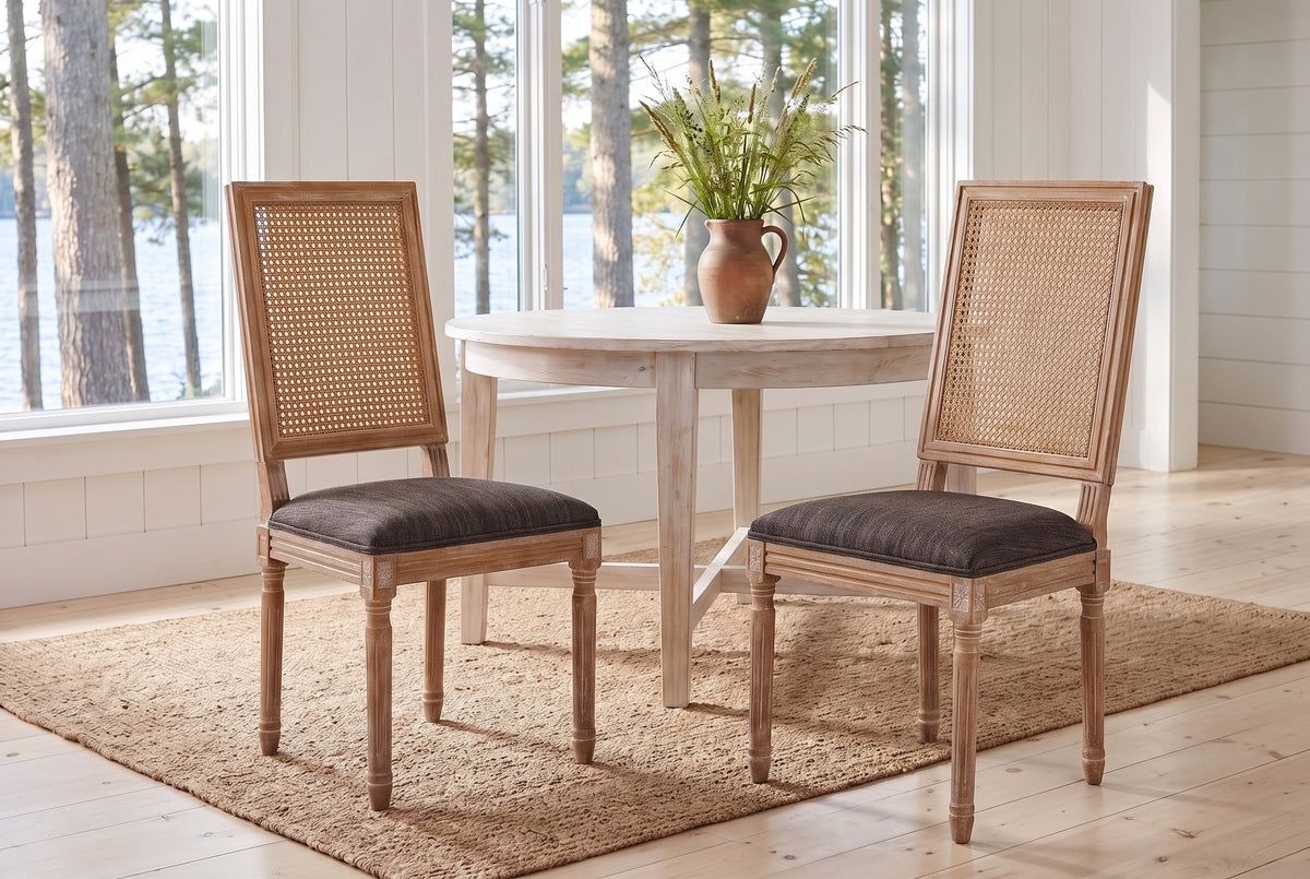 A pair of Castelfranco dining chairs in Brown on a jute rug in a white Muskoka cottage with a round table and the lake behind