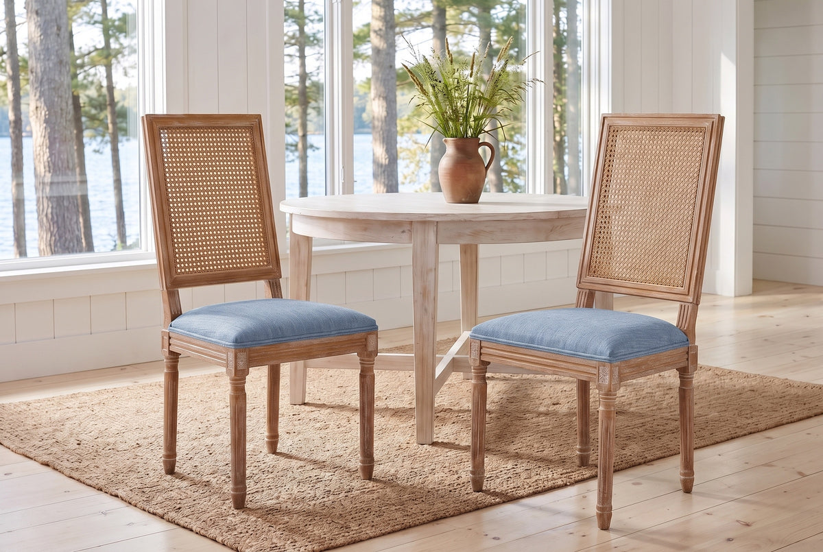 A pair of Castelfranco dining chairs in Denim Blue on a jute rug in a white Muskoka cottage with a round table and the lake b