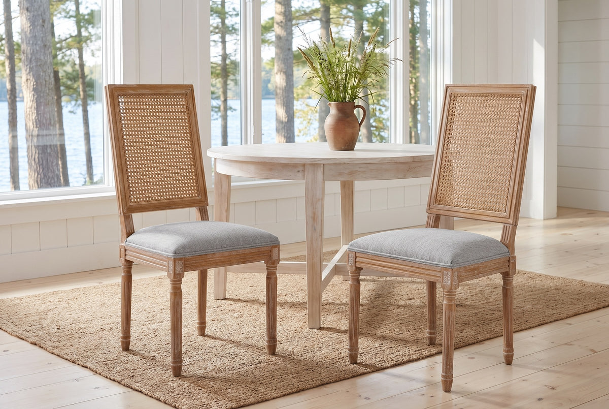 A pair of Castelfranco dining chairs on a jute rug in a white Muskoka cottage with a round table and the lake behind