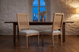 A pair of Castelfranco dining chairs in a whitewashed stone dining room in Quebec City at dusk, in front of a walnut table