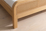 Close-up of the footboard corner curving into a square wood leg, with the woven panel and its thin bead