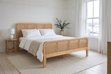 Certaldo cane bed made up with white linen in a bright bedroom with a harbour view and eucalyptus in a stoneware jug