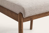 Close-up of a Cervo front leg in walnut: its rounded top beside the corner of the beige woven seat