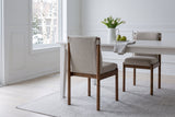 Cervo dining chair in beige and walnut from behind at a white table in an Ottawa dining room