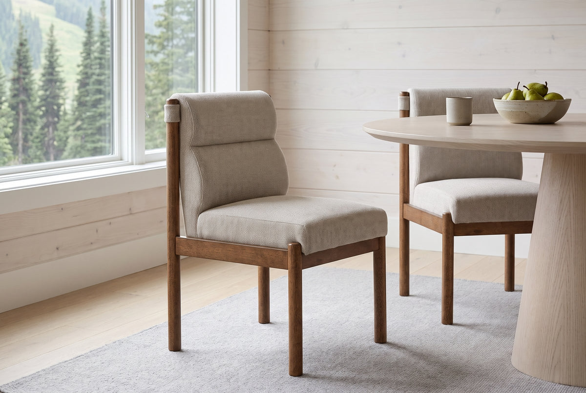 Two Cervo dining chairs in beige and walnut beside a round light ash table in a Whistler dining room with white spruce walls