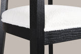Close-up of the ivory boucle-look seat, the black wood seat frame and a tapered front leg of the Black Cesena chair