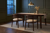 Two Cesena dining chairs at a dark walnut table in an olive-green Toronto dining room at dusk, under a brass pendant lamp