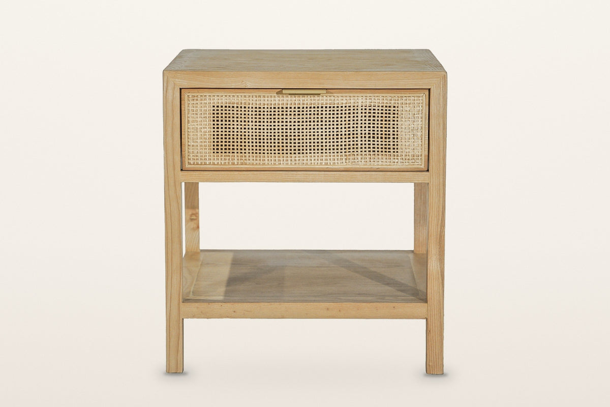 Cetara side table in Natural, front view on a warm white studio backdrop: the wicker drawer with a slim brass pull on its top