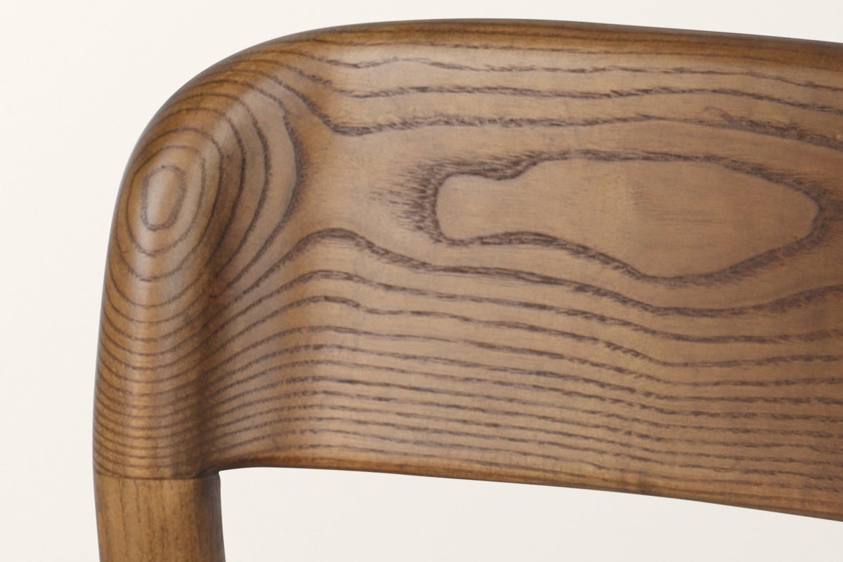 Close-up of the Chiavenna back rail in walnut: bold ash grain and the rounded end that caps the back leg