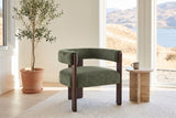 Chioggia accent chair in Olive Green by a lake-view window with a travertine side table and an olive tree