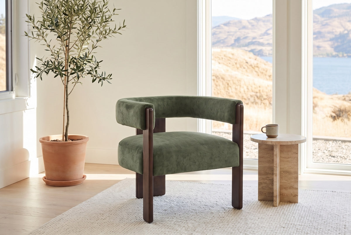 Chioggia accent chair in Olive Green by a lake-view window with a travertine side table and an olive tree