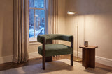 Chioggia accent chair in a townhouse reading corner at dusk, a brass floor lamp lit beside it (Olive Green)