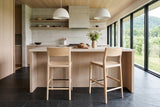 Two Cison counter stools in Natural seen from behind at a cream limestone island in a Saint-Hilaire orchard house