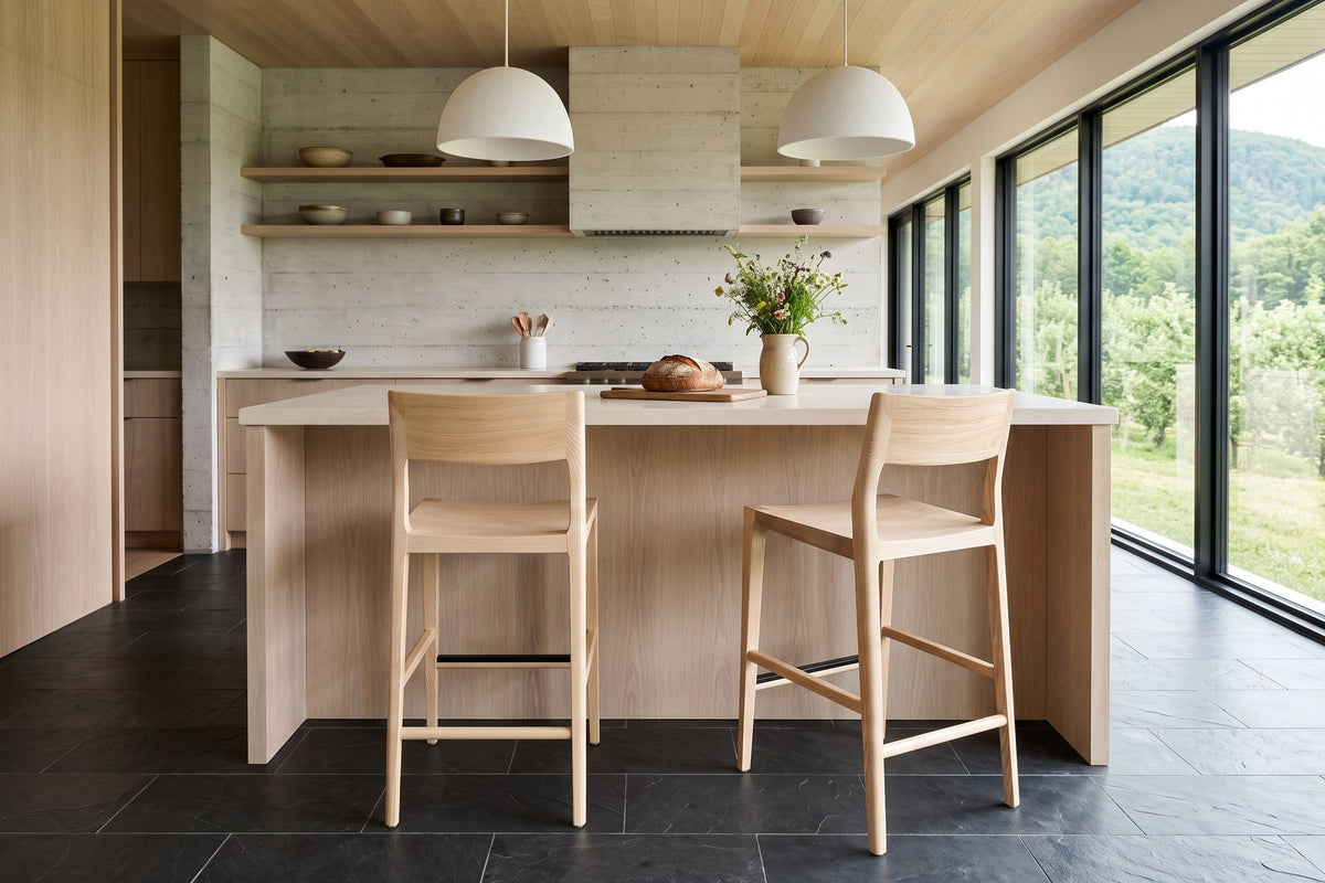 Two Cison counter stools in Natural seen from behind at a cream limestone island in a Saint-Hilaire orchard house