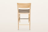 Cison counter stool in Natural from behind on a warm white studio backdrop: the outer face of the curved backrest and the rou