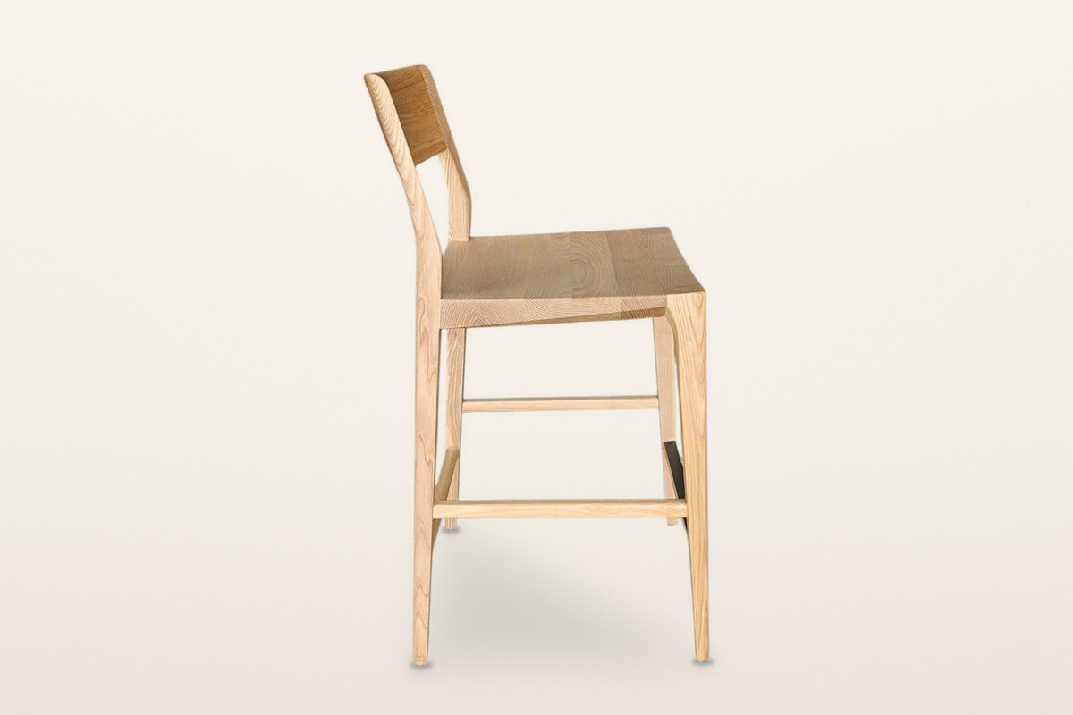 Cison counter stool in Natural, side view on a warm white studio backdrop: the back posts lean back above the seat and run do