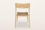 Cison dining chair in Natural, back view on a warm white studio backdrop: the backrest panel and the two posts