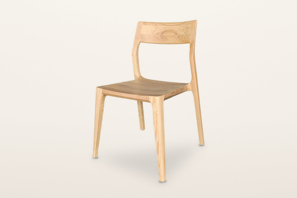 Cison dining chair in Natural, three-quarter view on a warm white studio backdrop: solid ash, one wide curved backrest