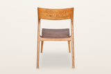 Cison dining chair in Warm Brown, back view on a warm white studio backdrop: the backrest panel and the two posts