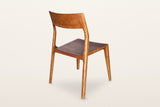 Cison dining chair in Warm Brown, rear three-quarter view on a warm white studio backdrop: the back of the backrest and the o