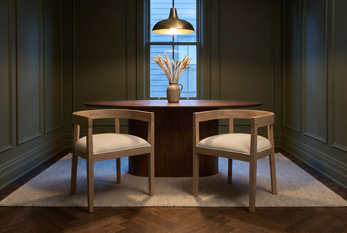 Two Civita dining chairs facing the camera at a walnut oval table in an olive-green panelled Toronto dining room at dusk