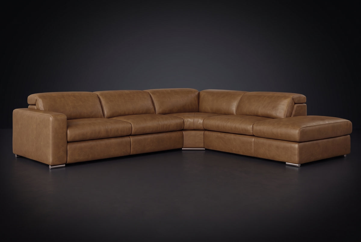The Clara sectional against a dark studio backdrop, headrests down, the chaise on the right. Shown in distressed full-aniline leather, Weathered Saddle, Right bumper.