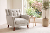 Comacchio armchair in beige beside a pale oak side table in a bright garden room with ferns and an olive tree