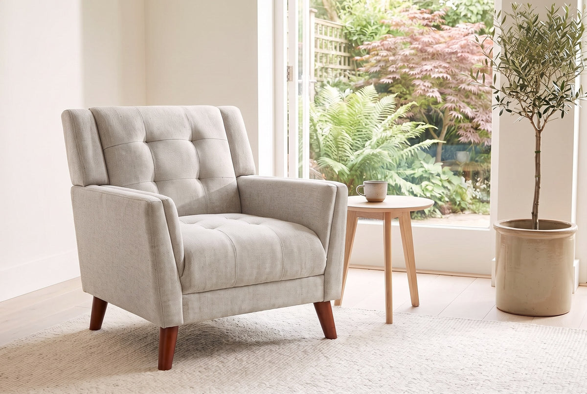 Comacchio armchair in beige beside a pale oak side table in a bright garden room with ferns and an olive tree