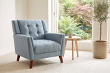Comacchio armchair in blue beside a pale oak side table in a bright garden room with ferns and an olive tree