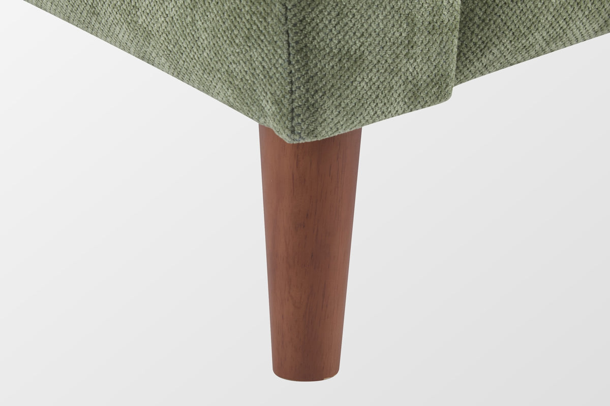 Close-up of a tapered solid wood leg in a walnut finish under the green chenille front corner