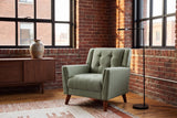 Comacchio armchair in green in a brick-walled loft with steel windows, a walnut sideboard and a black floor lamp
