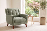 Comacchio armchair in green beside a pale oak side table in a bright garden room with ferns and an olive tree